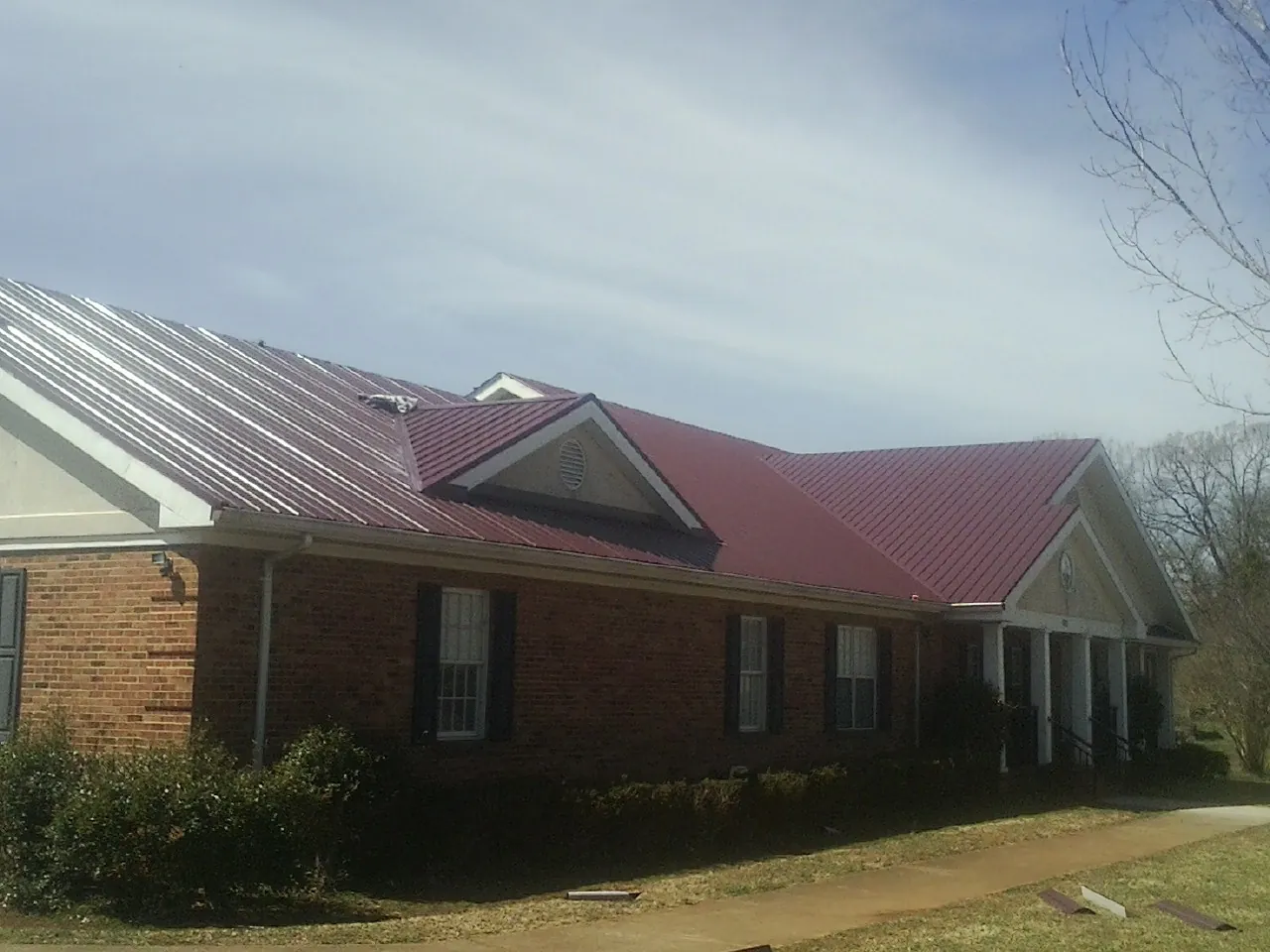 Red metal roof with gabled entries on a long brick building, from a Hail Damage Roof Repair job in Hollis