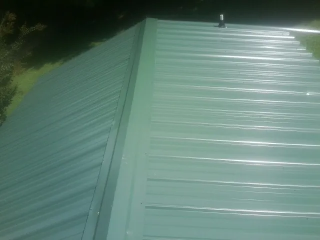 New green metal panels meeting at the ridge of a roof — Flat Roof Repair work by our crew in Hollis