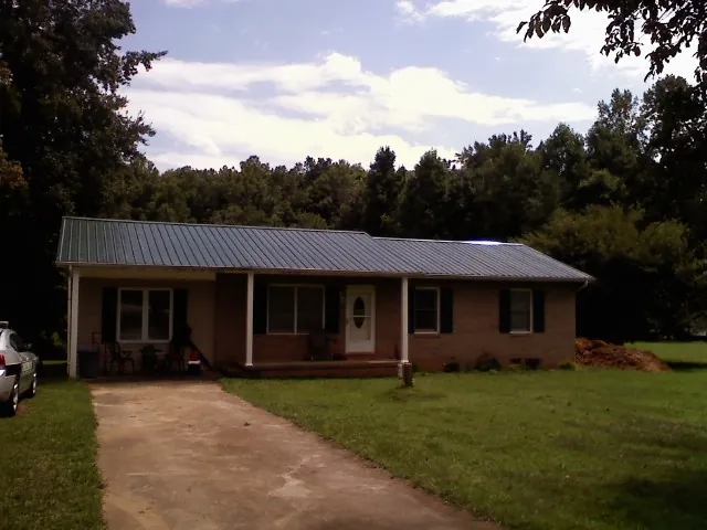 Dark green metal roof on a brick ranch with a covered porch in Hollis