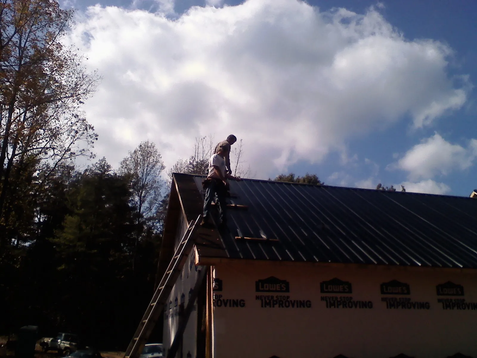Roofer fastening dark metal panels high against a cloudy sky, from a Roof Inspection job in Hollis