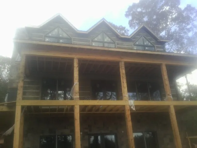 Dormers and porch framing on a large log home under construction — Roof Coating work by our crew in Hollis