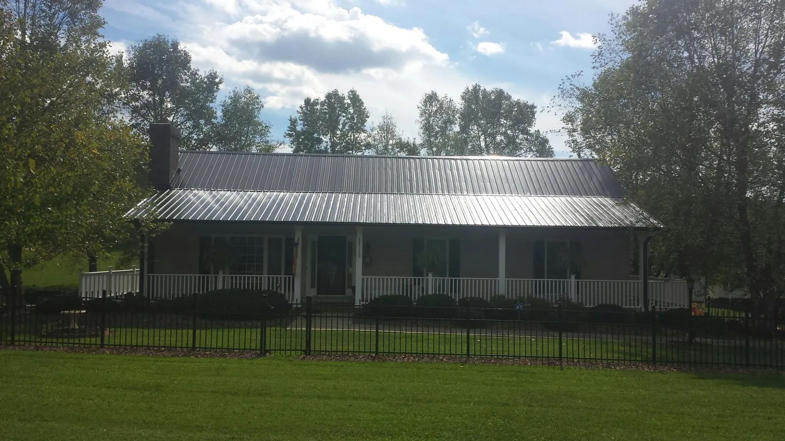 Gray metal roof on a brick ranch with a full width front porch — Gutter Guard Installation work by our crew in Hollis