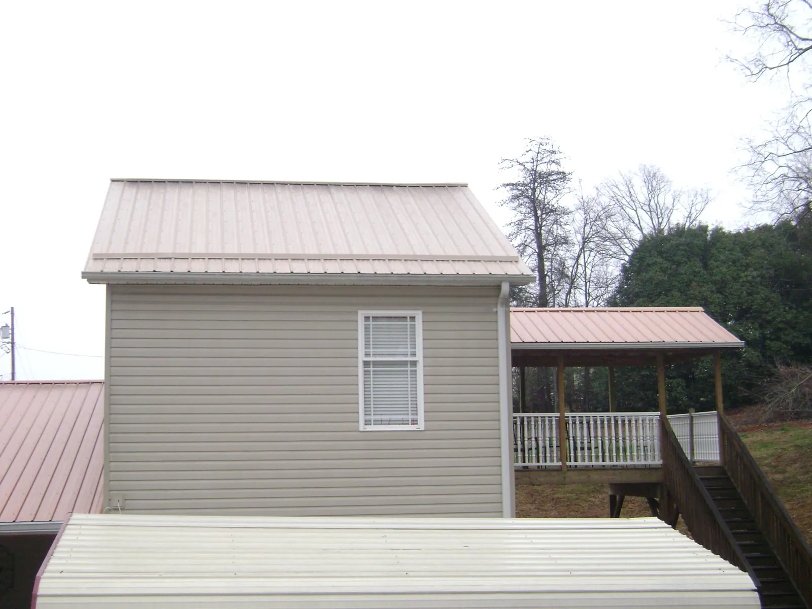 Tan metal roofs on a two story addition and attached porch, from a Roof Replacement job in Hollis